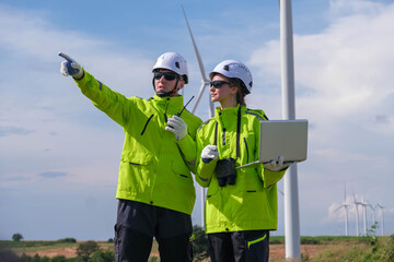 Engineers inspect wind farm and analyze data on laptop under clear sky