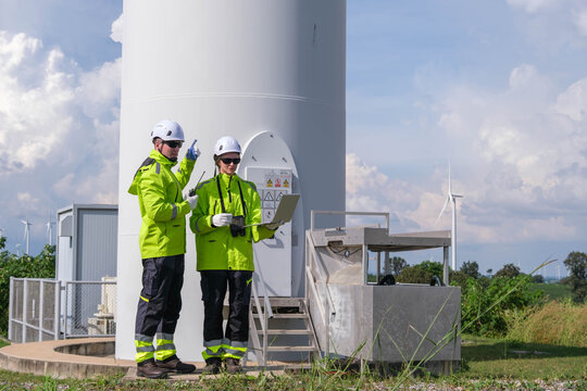 Technicians checking equipment at a wind turbine site during a sunny afternoon - Powered by Adobe