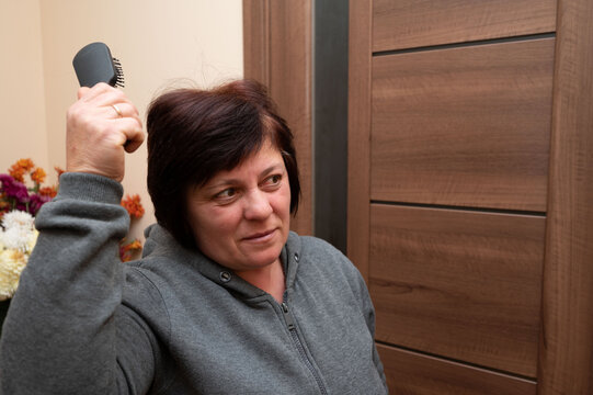 Woman preparing for a friendly gathering while brushing her hair in a cozy room with warm tones and vibrant floral decorations in the background