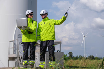 Engineers inspecting wind turbine site while using computer and radio for communication on a sunny day