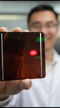 Close-up of glossy red transparent perovskite solar cell on glass substrate held by Chinese scientist in white lab uniform