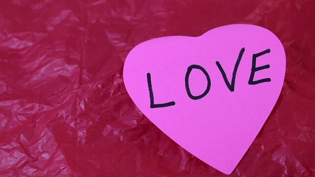 Un primer plano de una nota con forma de coraz&oacute;n con la palabra amor en un fondo rojo