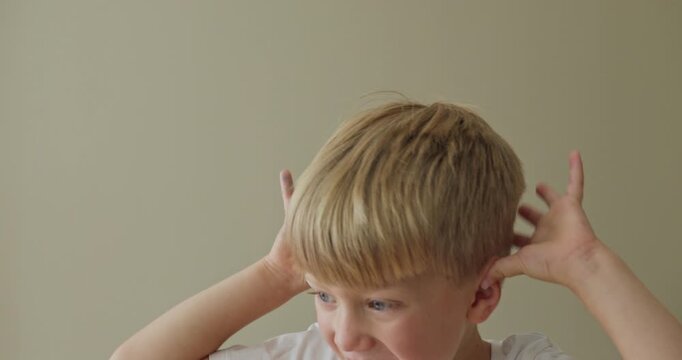 A boy is making funny faces at the camera, holding both hands to his ears and sticking out his tongue.