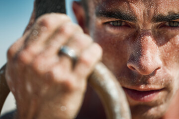 Sand-dusted athlete gripping gym rings in intense close-up, focused gaze and gritty determination captured during an outdoor strength workout
