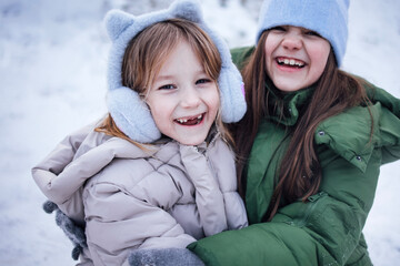 Obraz premium Two joyful young girls, one in a cozy pink jacket and the other in a green coat, are laughing together in a snowy landscape, capturing the essence of winter fun and friendship