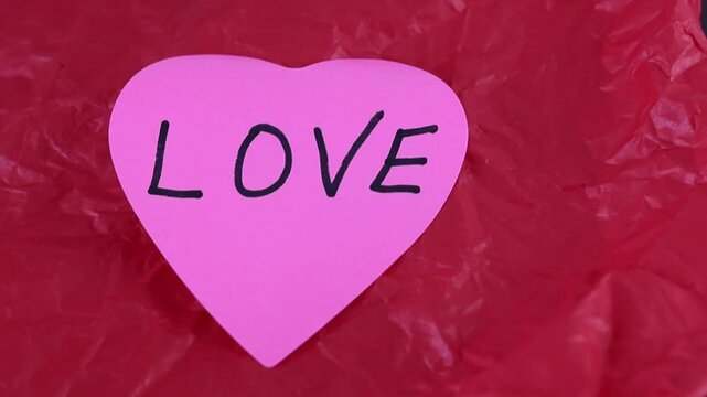Un primer plano de una nota con forma de coraz&oacute;n con la palabra amor en un fondo rojo