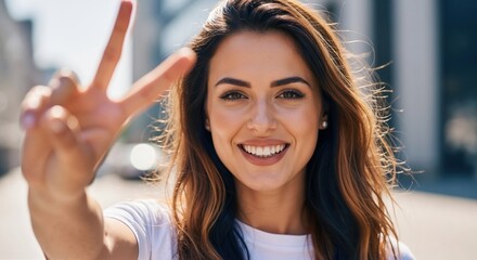 Happy young woman showing peace sign with hand. Smiling brunette female making victory gesture outdoors. Positive emotion concept