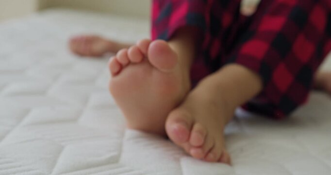 Close-up of a boy bare feet lying on the bed, one foot kicking against the other.