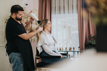 A hairstylist uses a hairdryer to style a woman's hair in a chic salon. Soft lighting, pink drapes, and floral decor create a calm, pampering atmosphere.