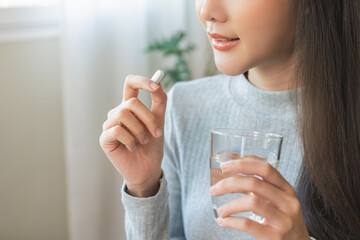 Dietary supplement, healthy diet positive asian young woman hand holding pill capsule, take vitamin in mouth for beauty skin hair, taking medicine with glass of water at home, pharmacy and health care