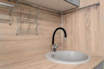 A fragment of a modern kitchen set with a sink and a flexible black faucet
