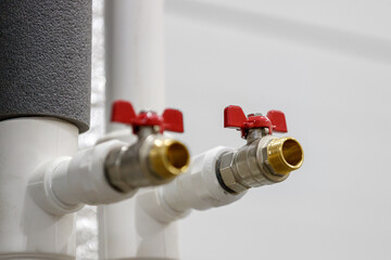 Two ball valves with red handles are installed on the plastic pipes of the water supply system