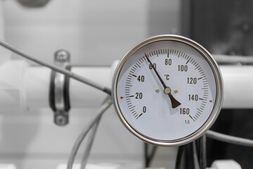 A round analog thermometer on industrial equipment shows a temperature above 60 degrees Celsius