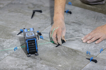 The process of laying floor tiles using a laser level and plastic wedges for leveling