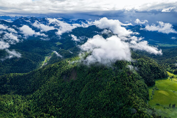 Aerial view of lush green forests meeting the clouds, with the majestic mountains in the distance, Berchtesgaden, Bayern, Germany.