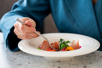 Hands eating gourmet raw fish appetizer with fork at restaurant.