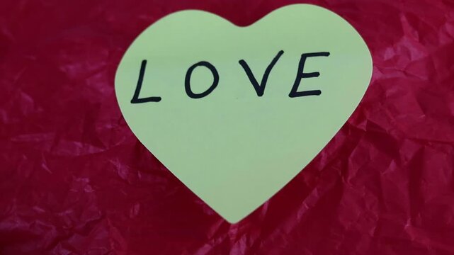 Un primer plano de una nota con forma de coraz&oacute;n con la palabra amor en un fondo rojo