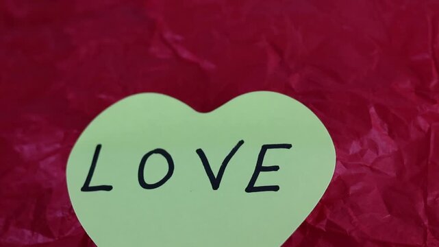 Un primer plano de una nota con forma de coraz&oacute;n con la palabra amor en un fondo rojo