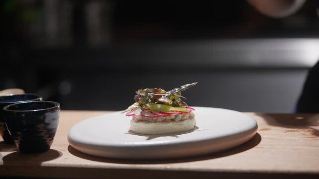 A chef is preparing a dish with a fork. The dish is on a white plate and has a garnish on top