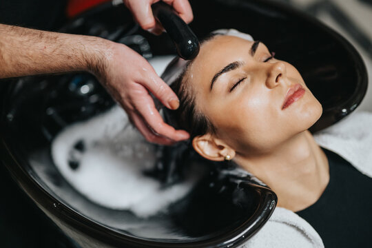 A client enjoys a soothing hair wash at a contemporary salon, with a stylist washing hair at a basin. Soft lighting and bubbles create a calm, pampering spa moment.