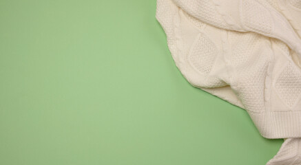 The edge of a white knitted sweater, located in the upper right corner, on a light green background.
