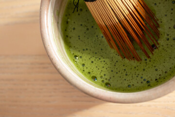 Creamy matcha tea whisked with bamboo chasen in traditional ceramic bowl, close-up. Slow living, mindful rituals, ceremonial matcha, natural ingredients, and modern tea culture