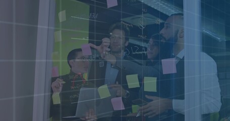 Planning colleagues in suits writing on glass wall in meeting area, using laptop and sticky notes