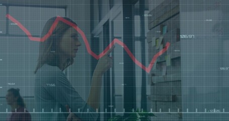 Using smartphone, woman in blouse consulting sticky-note wall in office with red chart overlay