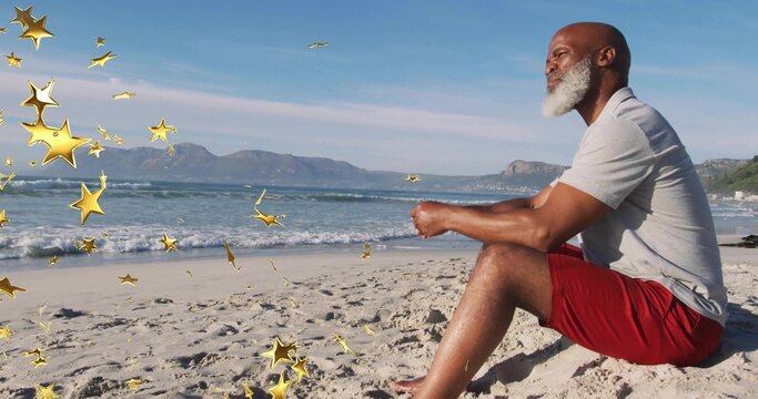 Sitting senior man facing ocean on beach with gold star overlay in gray-polo red-shorts, copy space