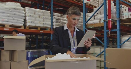 Inspecting manager in blazer and collared shirt using tablet, checking box at warehouse, pallets