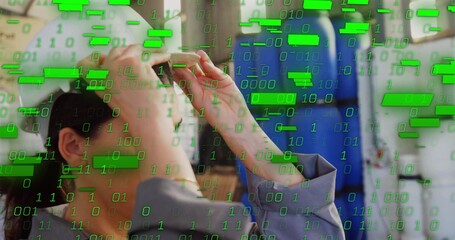 Female technician adjusting AR headset in technology factory, with floating binary code overlay
