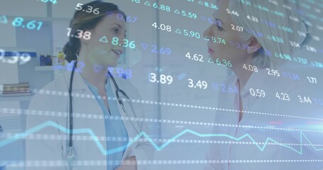 Discussing two female doctors reviewing in clinic, wearing lab coats, stethoscope, overlaid data