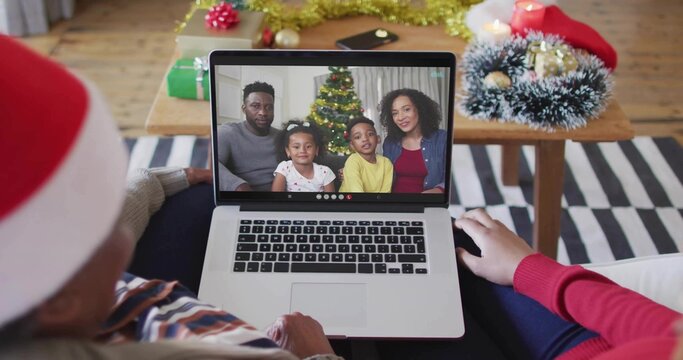 Watching two adults on couch sharing laptop in living room, with Santa hat, red sweater, gifts
