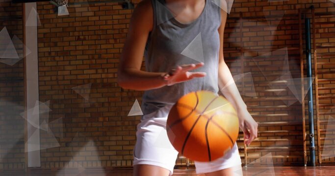 Dribbling teenage female wearing gray tank and white shorts in school gym, with orange basketball