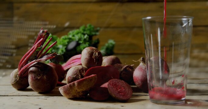 Pouring bright beet juice into tall clear glass on rustic wooden table, with halved beets