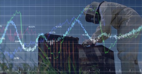 Inspecting technician in protective suit operating instrument on sealed crate, financial overlay