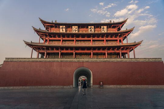 Honghe, China - 22 November 2025: View of the ancient gate, its red walls standing strong against the soft sky, framing a distant figure walking through the archway.