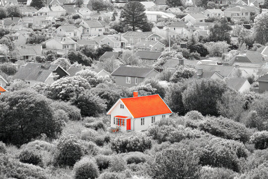A striking red-roofed house stands out amidst a sea of monochrome homes and greenery, creating a vivid contrast in the landscape. - Powered by Adobe