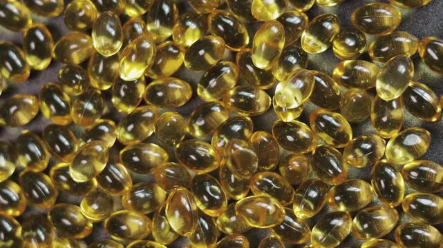 Top-down, close-up video of golden softgel capsules, like vitamin or fish oil supplements, slowly rotating on a turntable on black background showing concepts of healthcare, medicine, and nutrition.