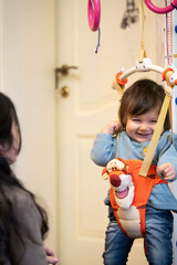 Joyful moments of a toddler bouncing happily in a playful harness while a caring adult interacts with excitement in a cozy indoor setting