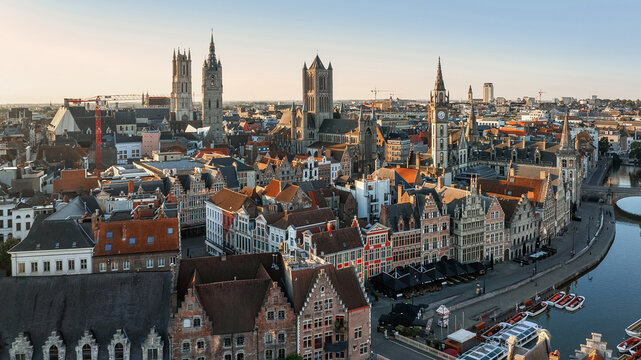 Aerial view of the skyline dominated by the iconic towers of Saint Bavo Cathedral and Ghent Belfry, casting long shadows over the medieval rooftops, Ghent, Flanders, Belgium.