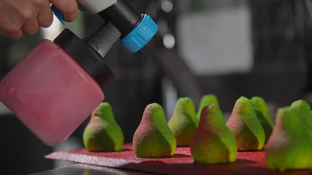 A tray of green pear-shaped cookies sits on a red cutting board. The cookies are arranged in a row, with some of them overlapping each other. The tray and cutting board are placed on a countertop
