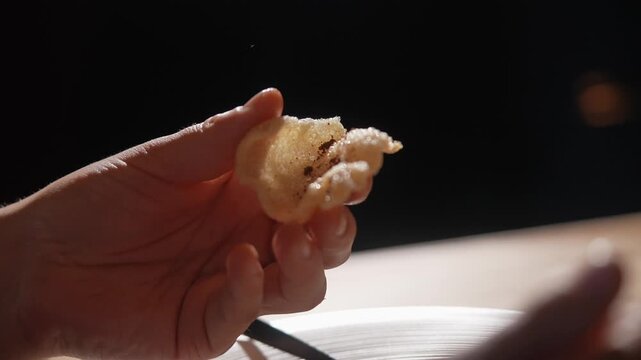 A hand holding a piece of food. The food is a small, crispy, and possibly fried item. The hand is positioned in a way that it is about to take a bite of the food