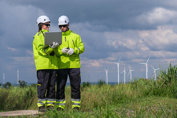 Engineers review project data while standing in a wind farm under a cloudy sky during daytime