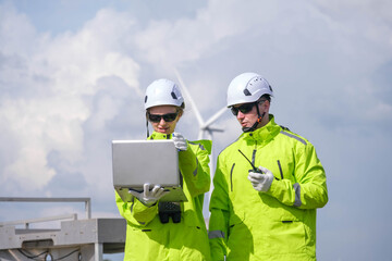 Engineers in bright jackets using laptop at wind farm site on a sunny day, collaborating on energy solutions