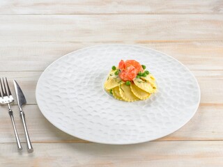 A beautiful serving of grialsoli pasta features tender shapes adorned with vibrant shrimp and peas. The dish rests on an elegant textured plate, set on a light wooden table