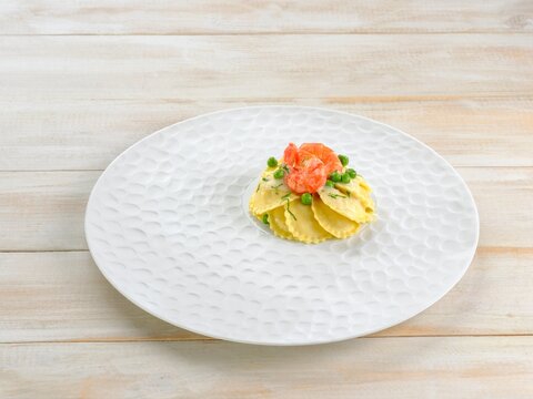 Chefs skillfully prepare Griasoli Pasta adorned with fresh shrimp and vibrant green peas. The dish sits elegantly on a white, textured plate, inviting a delicious dining moment