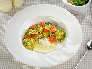 A bowl of Griasoli pasta is beautifully plated, adorned with cherry tomatoes and fresh herbs. The creamy sauce enhances its vibrant colors in a cozy dining atmosphere