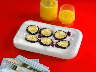 A plate of beautifully crafted Griasoli pasta is artfully arranged on a white platter. Fresh drinks sit nearby, enhancing this appetizing scene set against a bright red backdrop