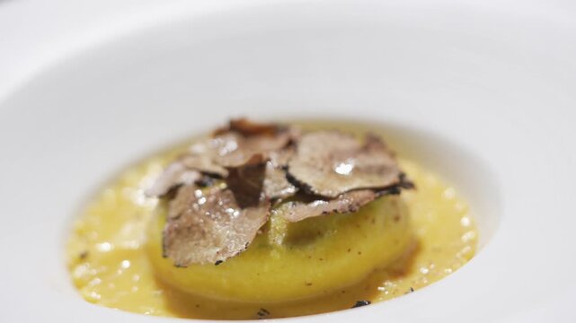 A plate of food with a yellow sauce and a white plate. The food is topped with black flakes